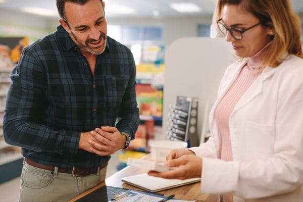 Pharmacist handing a prescription to a smiling customer at the pharmacy counter